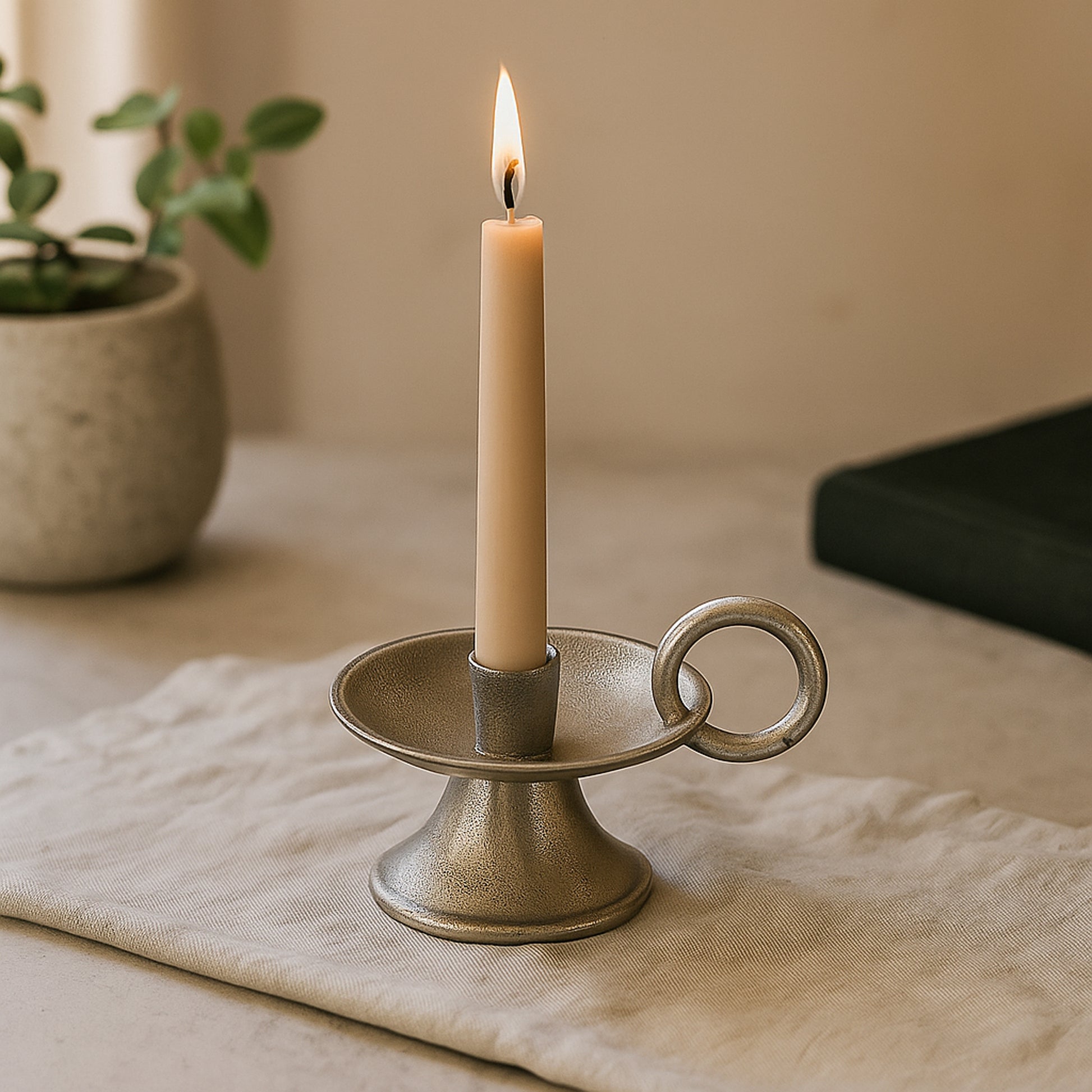 Candle in a decorative holder on a table with a plant in the background