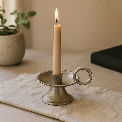 Candle in a decorative holder on a table with a plant in the background