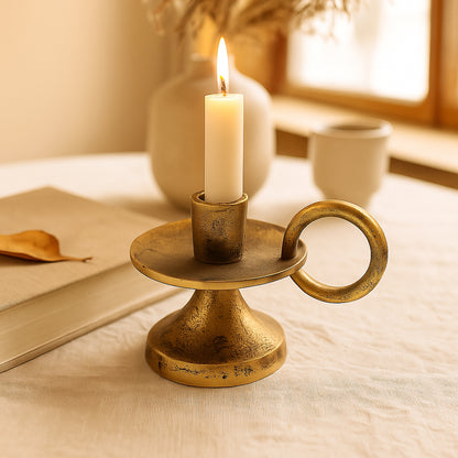 Brass candle holder with a lit candle on a soft surface with a warm light